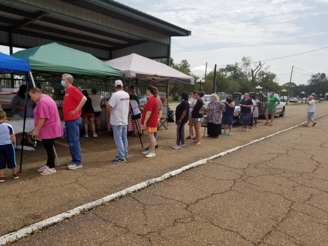 People wait in line under pop-up tents on cracked pavement at an outdoor K-12 online charter school event.