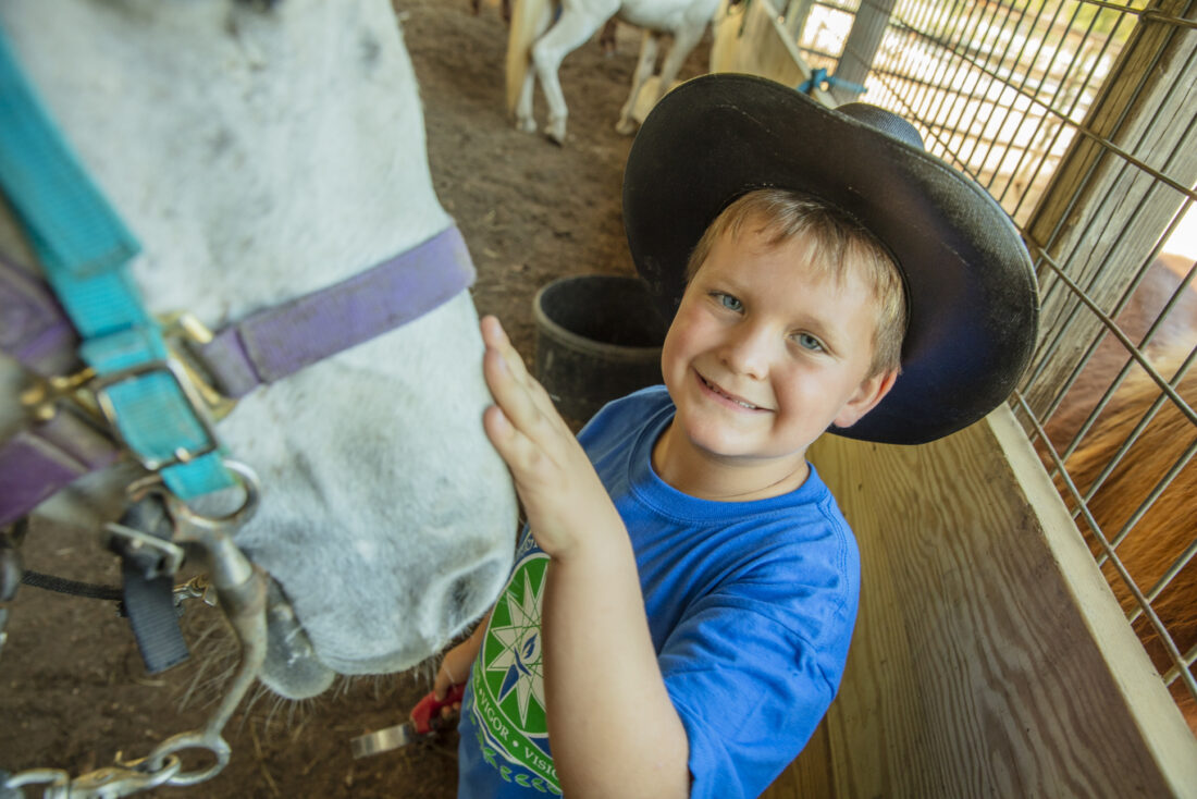 Young boy with cowboy hat petting his horse