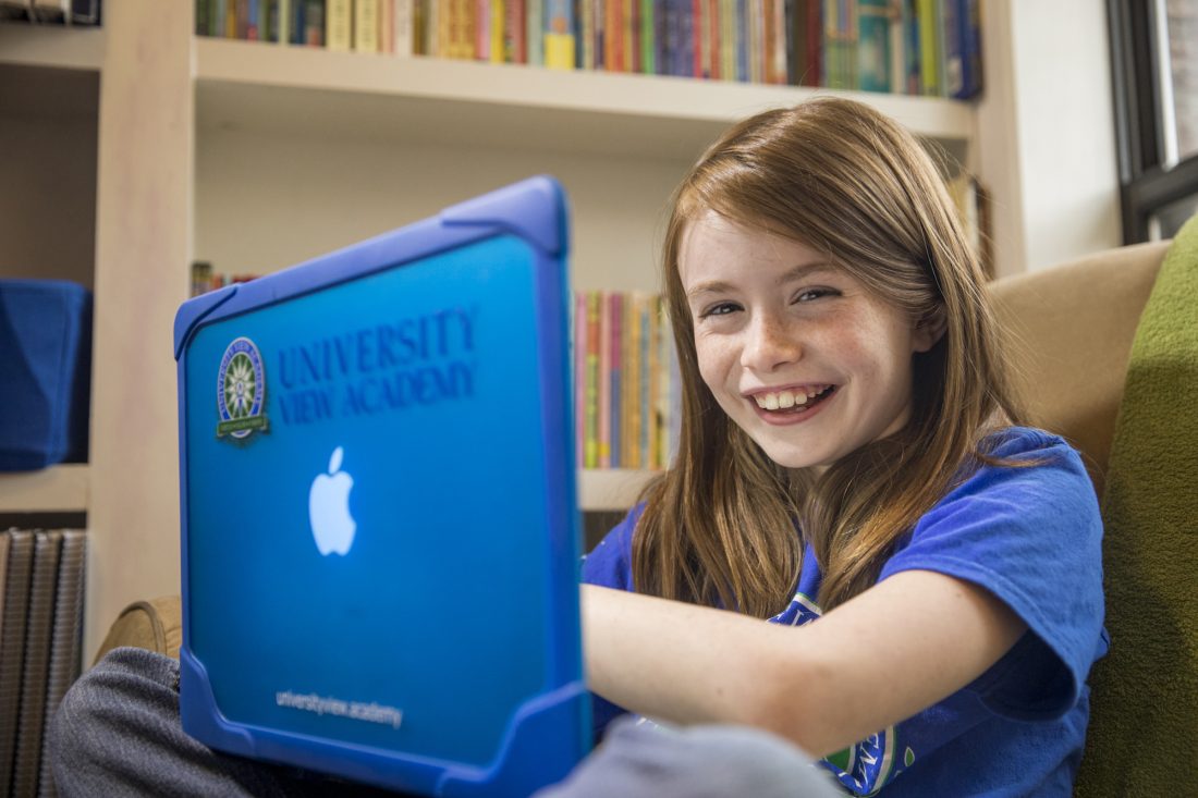 A smiling young girl in front of a laptop.