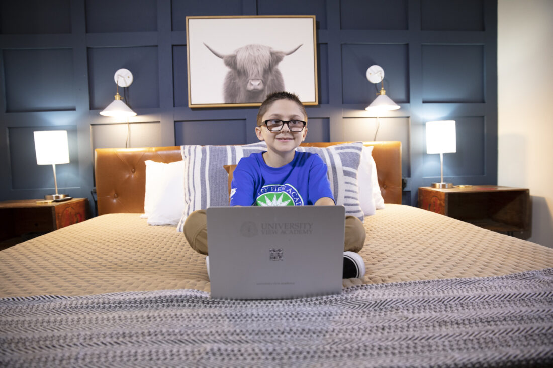 A boy working on his laptop on a bed.