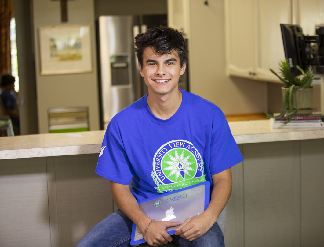 A teenage boy with a closed laptop, smiling for the camera.