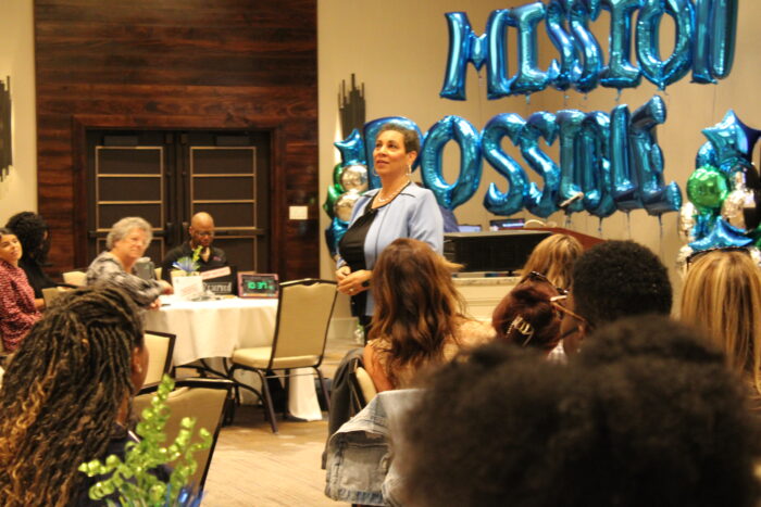 Merlyna Valentine speaking to audience in front of Mission Possible balloon arrangement