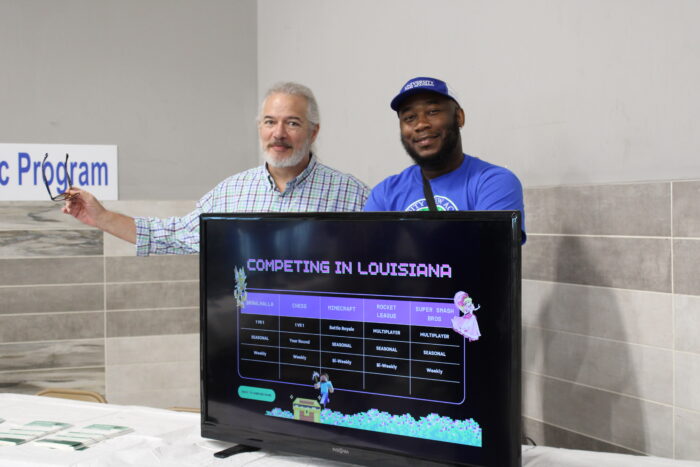 Two men standing behind a TV monitor with a video game on the screen.