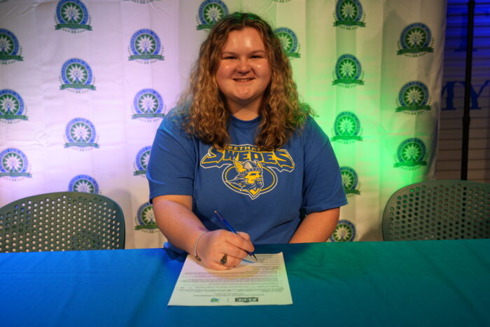 A girl sitting at a table, signing her letter of intent.