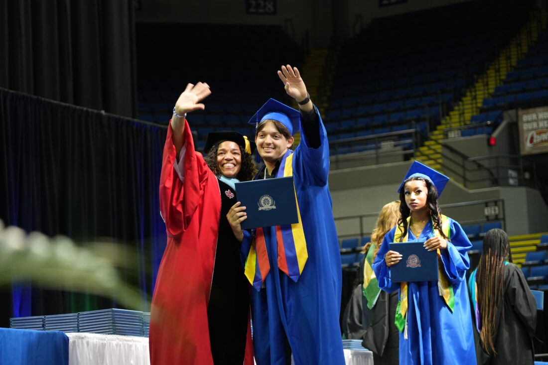 A student waves to family with Superintendent Dr. Quentina Timoll after receiving his diploma.