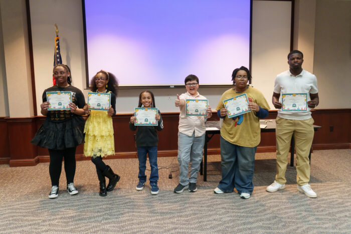Six students lined up in a row holding award certificates and smiling at the camera.