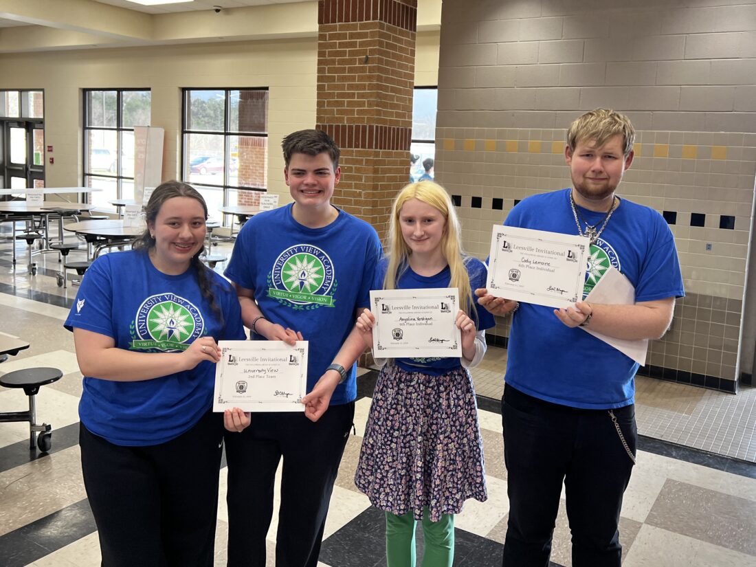 Four members of the UVA Quiz Bowl team, all dressed in UVA t-shirts, hold up their award certificates and smile for the camera.