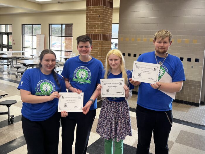 Four members of the UVA Quiz Bowl team, all dressed in UVA t-shirts, hold up their award certificates and smile for the camera.