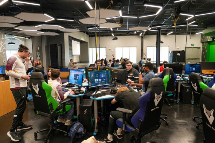 Students attend K-12 online charter school classes at computers in a modern gaming center with green chairs and monitors.