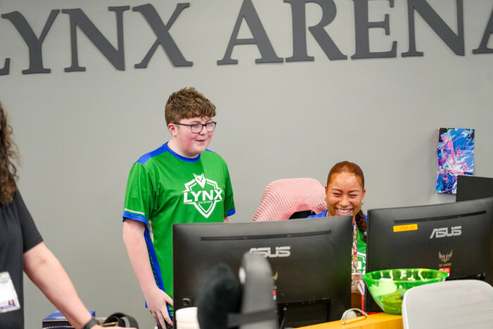 Two people smile while working at monitors in an office labeled 