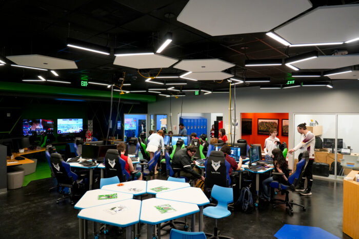 Students at computers in a bright, modern online school classroom with colorful chairs and large screens.