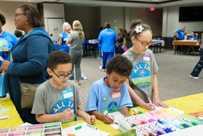 Three students color with markers at Literacy Day