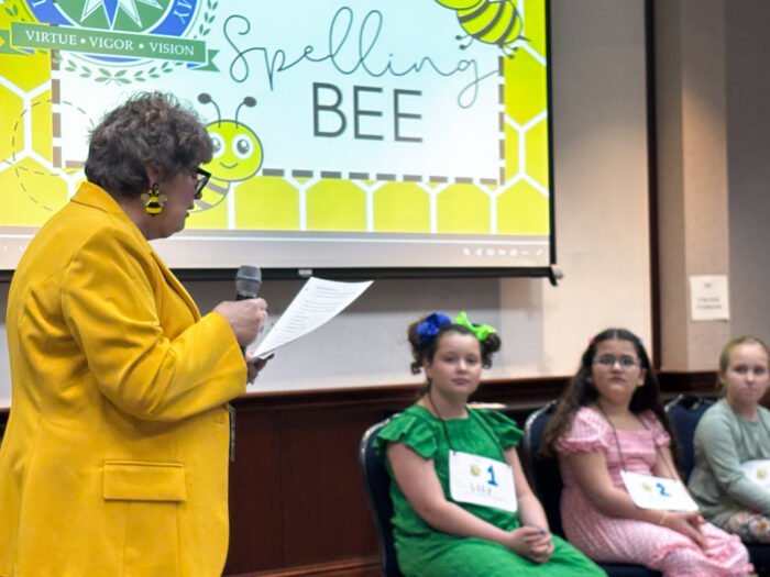 UVA teacher and club sponsor Sheryl Waltman reads words aloud to students at the spelling bee.