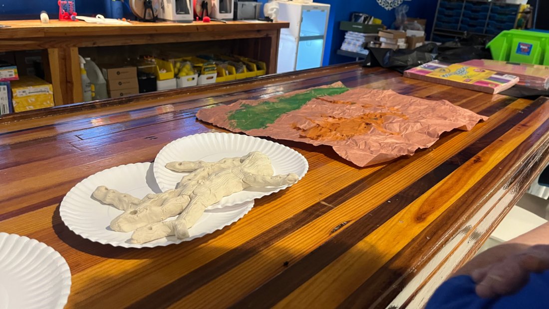Clay hand shapes on paper plates rest on a wooden counter near painted crumpled paper.