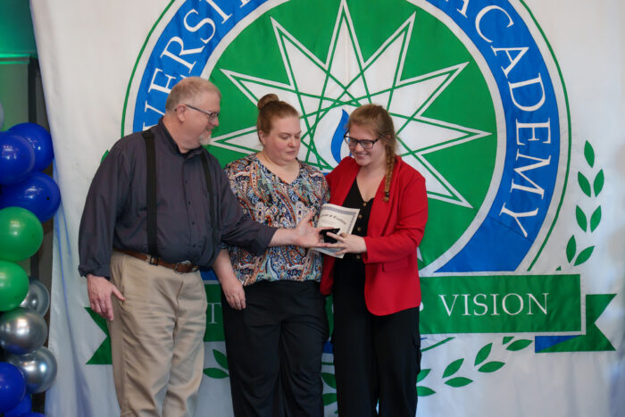 A student holds up a certificate and smiles for a picture with her parents