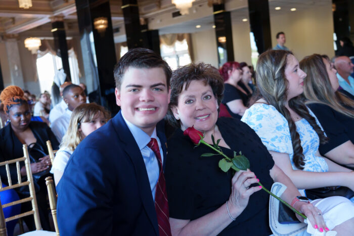 A student and his mother, who is holding a rose, smile for the camera