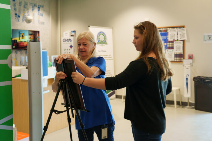 A teacher helps a student set up art on an easel.
