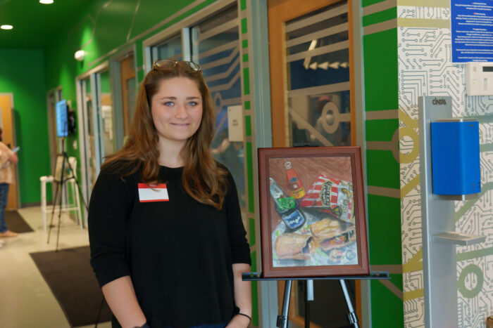 A student smiles for a picture next to her artwork
