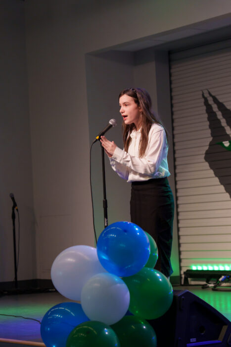 A student sings on the Lynx Den stage with a passionate expression.