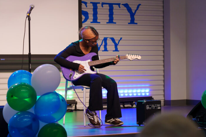 A seated student plays guitar on the Lynx Den stage.