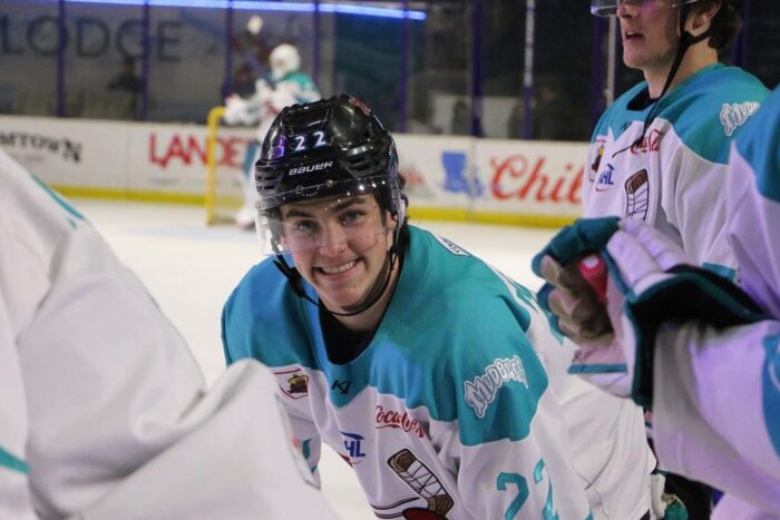 A smiling hockey player in a teal and white number 22 jersey balances K-12 online school with time on the ice.