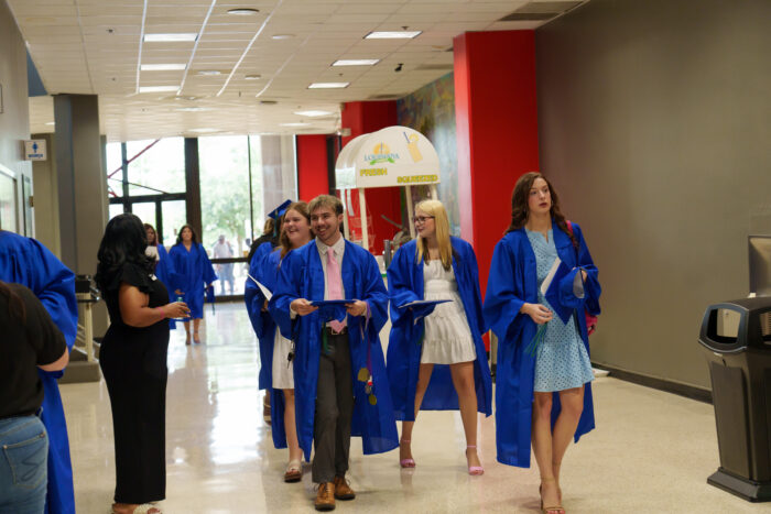 Students in blue graduation gowns walk down a hallway.
