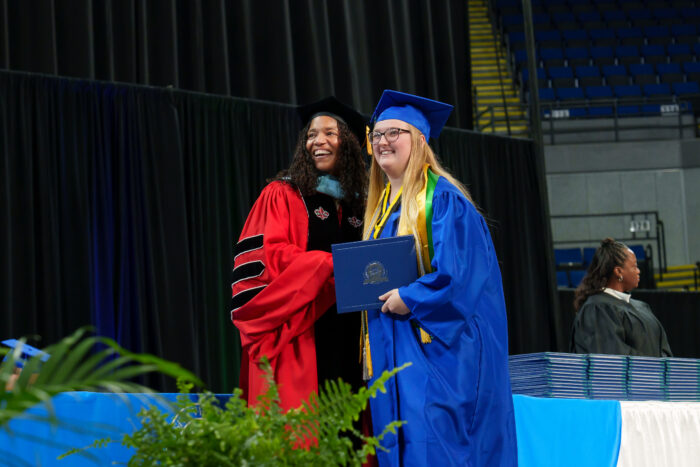 A graduate holds a diploma on stage and poses for a picture with Superintendent Timoll.