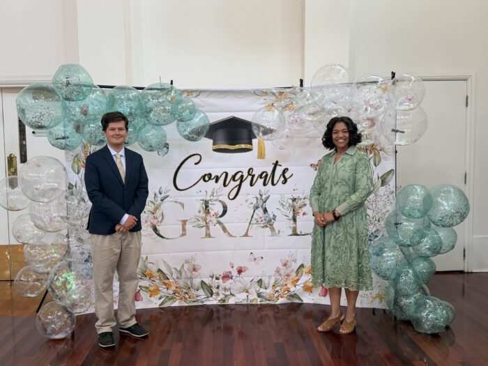 Charles Steele and Superintendent Timoll stand by a "Congrats Grad" banner and teal and white balloons at the Louisiana Association of Public Charter Schools luncheon.