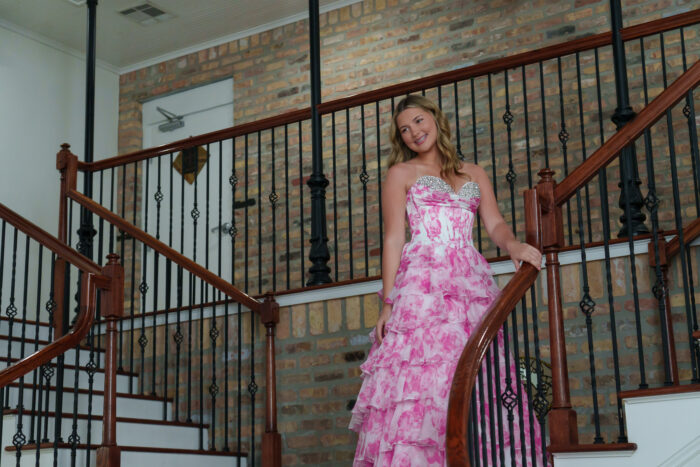 A student in a pink and white gown poses for a picture on a staircase.