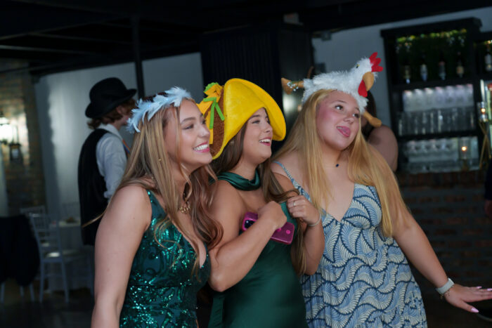 Three students in fun prop hats pose for a picture at the photo booth.