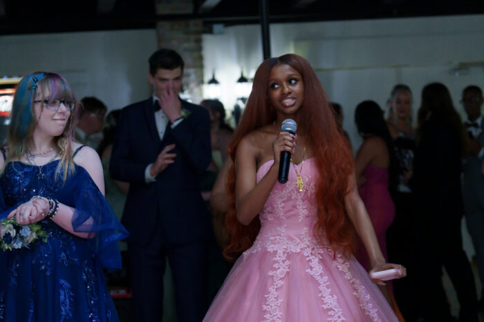 A student in a pink dress speaks into a microphone.
