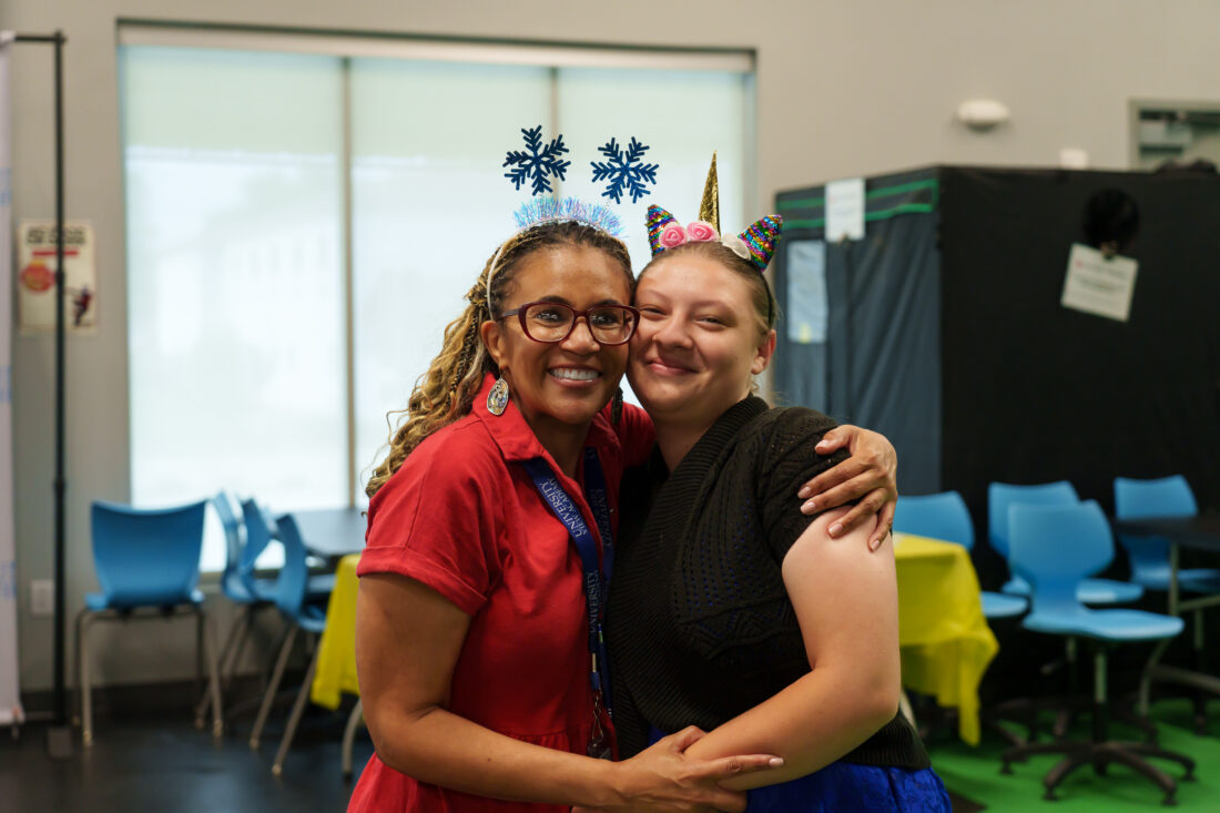 A teacher and a student embrace and smile for the camera.