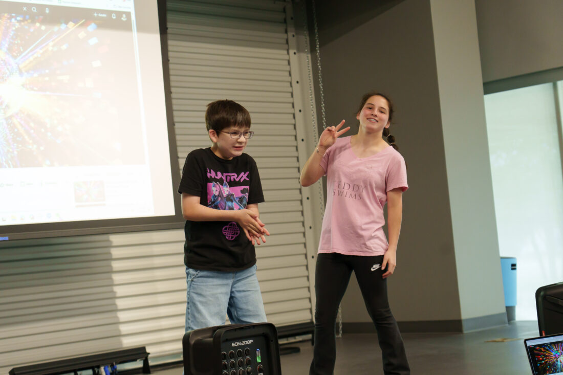 A boy and a girl on stage, the girl giving a peace sign to the camera.