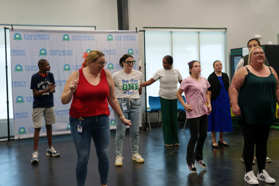 A group of students and teachers dance together energetically.