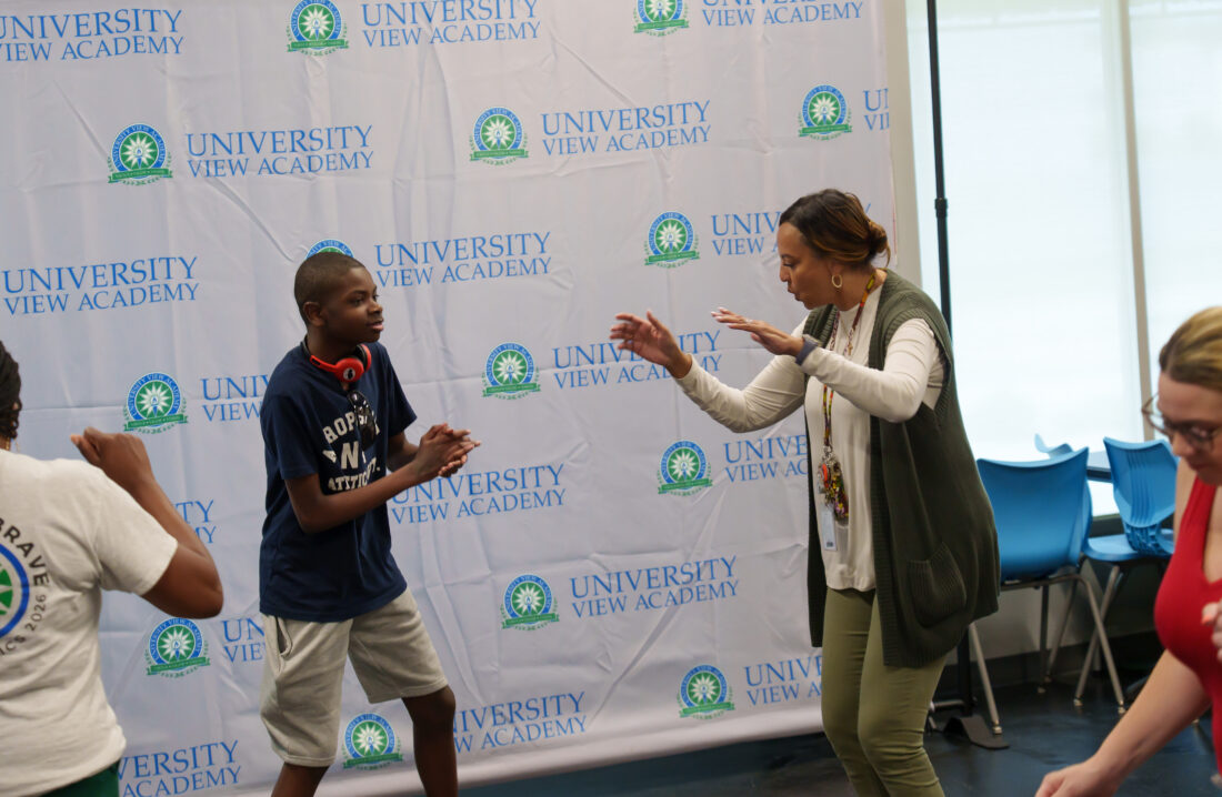 A teacher and a student dance together before a University View Academy backdrop.