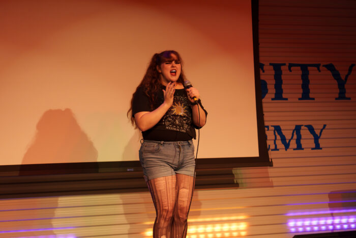 A student sings into a microphone on stage with a passionate expression.