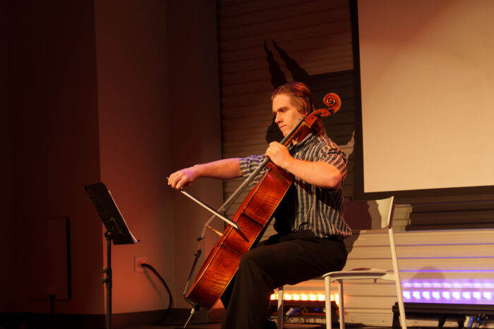 A seated student plays cello with a look of concentration.