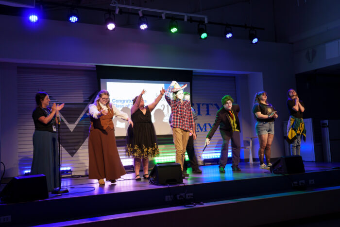 Students take a bow on a colorfully-lit stage.