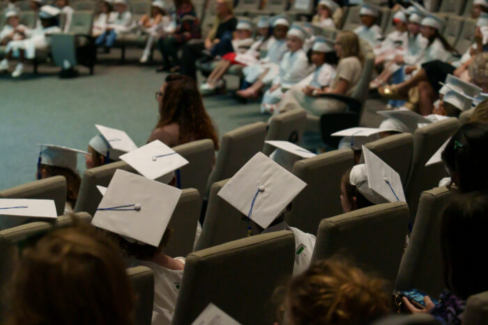 Kindergarten graduates in white caps and gowns sit in rows at University View Academy’s Class of 2026 ceremony.