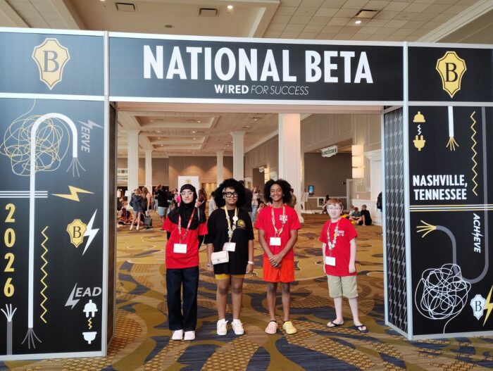 Four students in red shirts and badges stand under a 