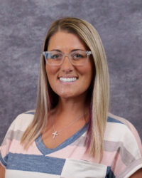 Abbie Dewitt headshot. Smiling woman with straight blonde hair, glasses, and a striped shirt against a gray mottled background.