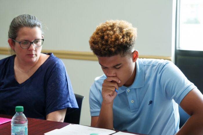A student fills out paperwork while an adult watches.