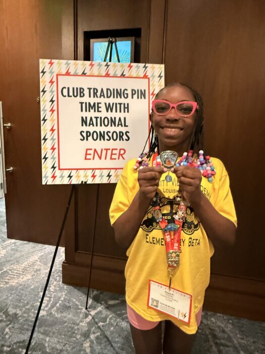 A smiling student stands by a sign, holding colorful pins and beads.
