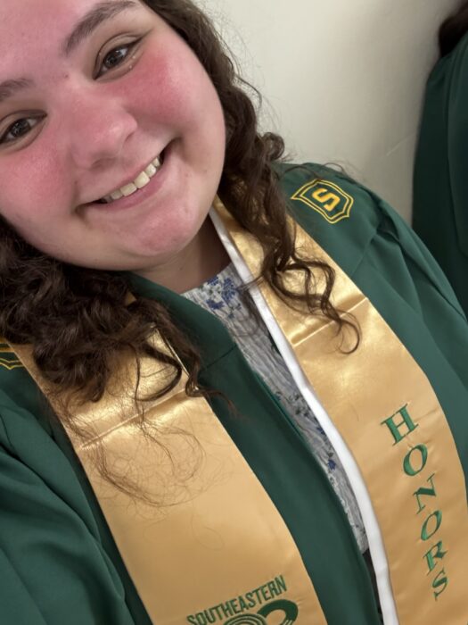 Barnett smiles at the camera in her college graduation gown and an honors stole.