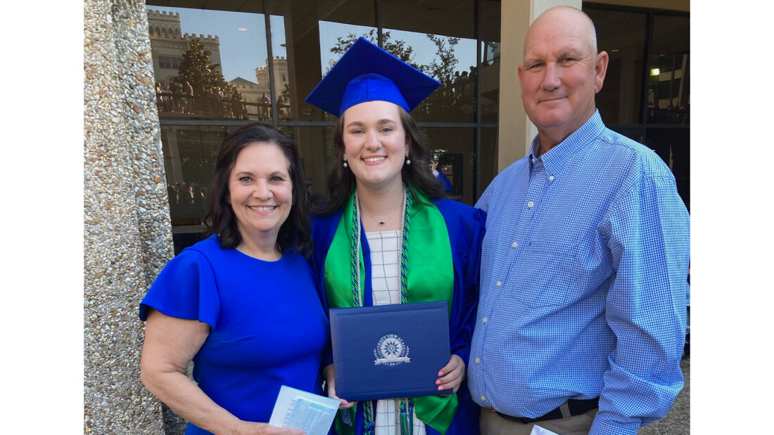 Lily Saucier in blue gown, grad cap, and green stole after graduation in 2022. Joined in picture by mother and father
