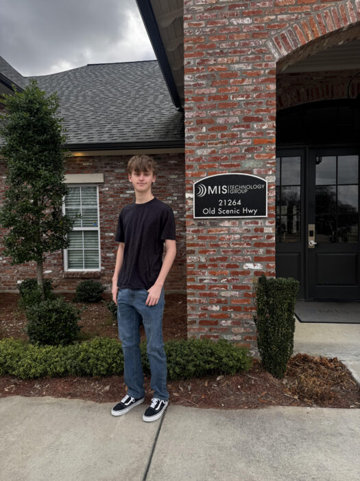 A student stands outside a brick building by a sign: 