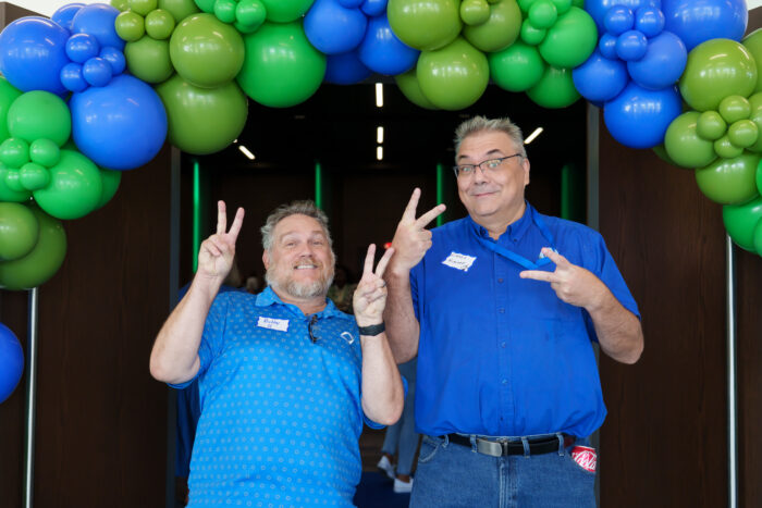 Two teachers smile for a picture under green and blue balloons.