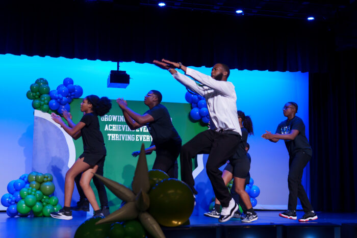 A teacher and several students dance on stage.