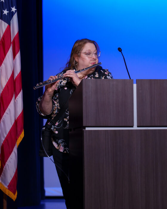 A teacher plays a flute behind a podium.