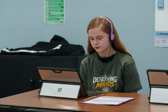 A student in headphones uses a laptop at a desk.